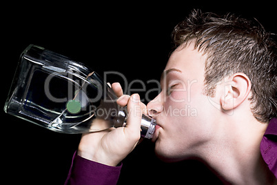 The young man drinks vodka from a bottle. Isolated on black