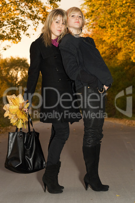 Two young blondes with autumn leaves on a road