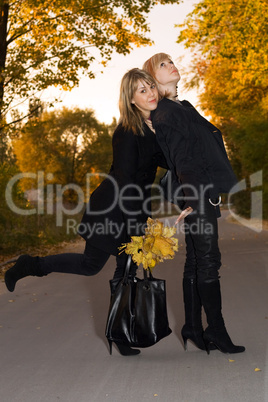 Two beauty young blondes with autumn leaves on a road