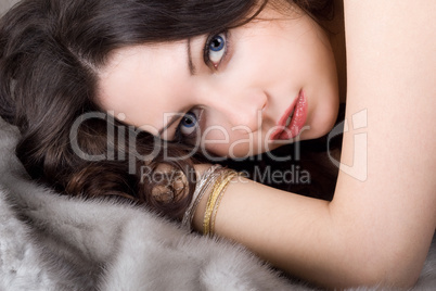 Lovely young woman lying on grey fur coat
