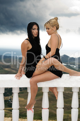 Two attractive young women sitting on a white handrail