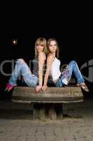 Two attractive girls sitting on a stone