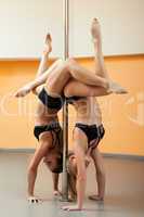 two athletic girl stand on hands during pole dance