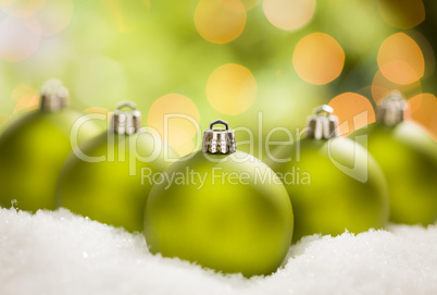 Green Christmas Ornaments on Snow Over an Abstract Background
