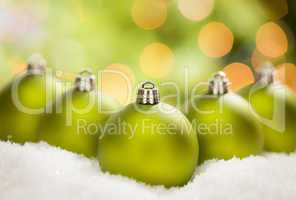 Green Christmas Ornaments on Snow Over an Abstract Background