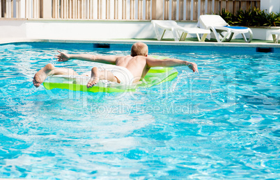 Junger mann auf einer grünen luftmatratze in einem schwimmbad