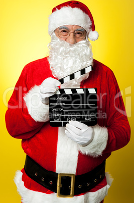 Cheerful Kris Kringle posing with clapperboard