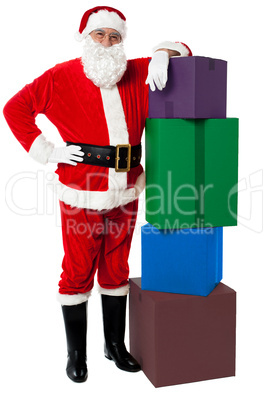 Santa Claus posing beside pile of gifts on Christmas eve