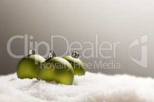 Green Christmas Ornaments on Snow Over a Grey Background