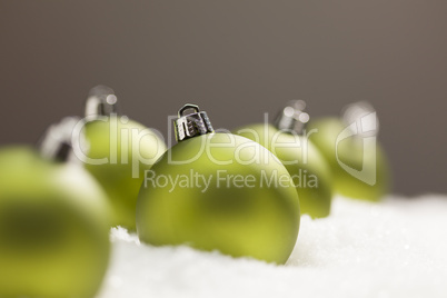 Green Christmas Ornaments on Snow Over a Grey Background