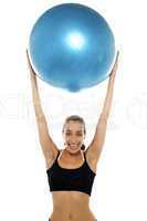 Fit young lady holding up big blue pilates ball