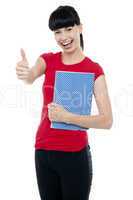 Pretty teenager holding notebook and gesturing thumbs up
