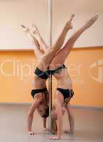 two athletic girl stand on hands during pole dance