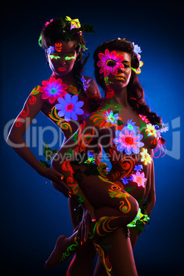 Nude women with glow uv body art and flowers