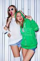 two beautiful young girls with red lollipops near the wall