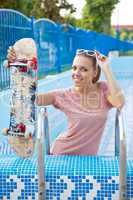 a beautiful young girl with a skateboard on the pool ladder