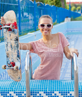 a beautiful young girl with a skateboard on the pool ladder