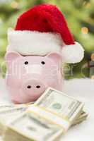 Pink Piggy Bank Wearing Santa Hat Near Stacks of Money on Snowfl