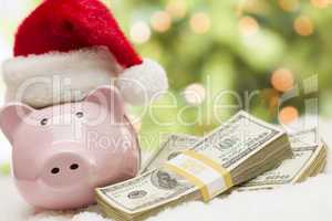 Pink Piggy Bank Wearing Santa Hat Near Stacks of Money on Snowfl