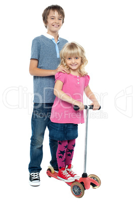 Brother holding her sister as she rides her toy scooter