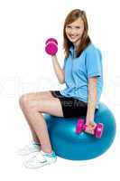 Pretty teen seated on a blue pilate ball doing dumbbells