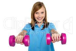 Adorable teen holding dumbbells in her outstretched arms