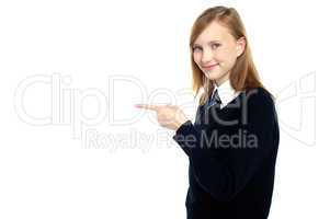 Pretty schoolgirl pointing towards copy space area