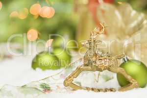 Golden Christmas Reindeer Ornament Among Snow, Bulbs and Ribbon
