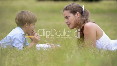 Mom helping son with homework, laying down on grass