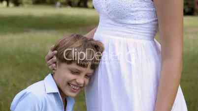 Happy pregnant mother with son leaning head on tummy