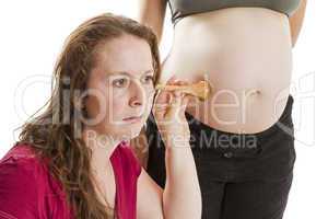 young midwife listening at pregnant human belly