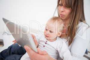 Serious woman holding her baby while using a tablet pc