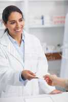 Smiling pharmacist handing paper to a customer