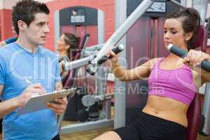 Trainer noting progress of woman using weights machine