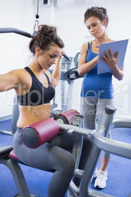 Female trainer taking notes on client on weights machine