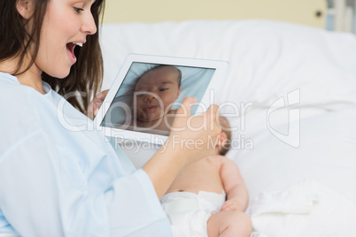 Smiling mother using a tablet to take a picture of a newborn bab