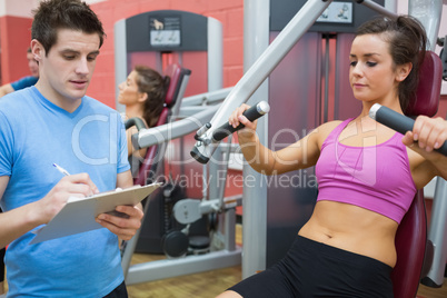 Trainer taking notes on client on weights machine