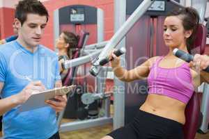 Trainer taking notes on client on weights machine