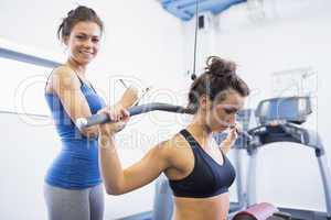 Smiling trainer with woman using weights machine