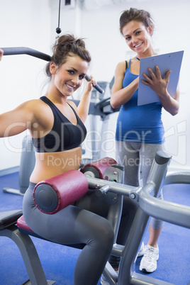 Happy female trainer and client on weights machine