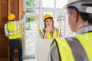 Woman and architect talking while man is measuring wooden frame