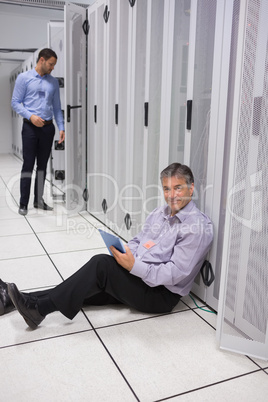 Smiling technician using tablet pc sitting on floor