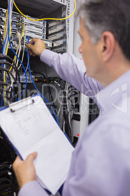 Technician fixing wires of server while holding clipboard