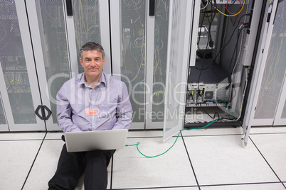 Smiling man doing server maintenance with laptop