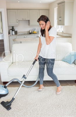 Woman standing holding a vacuum cleaner wearing headphones