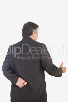 Mature businessman with fingers crossed offering handshake