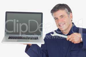 Mature mechanic holding wrench and laptop