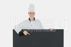 Happy female chef pointing at black billboard