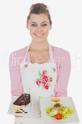 Woman in apron holding plates of pastry and healthy meal