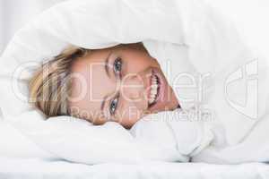 Happy woman hiding under the duvet